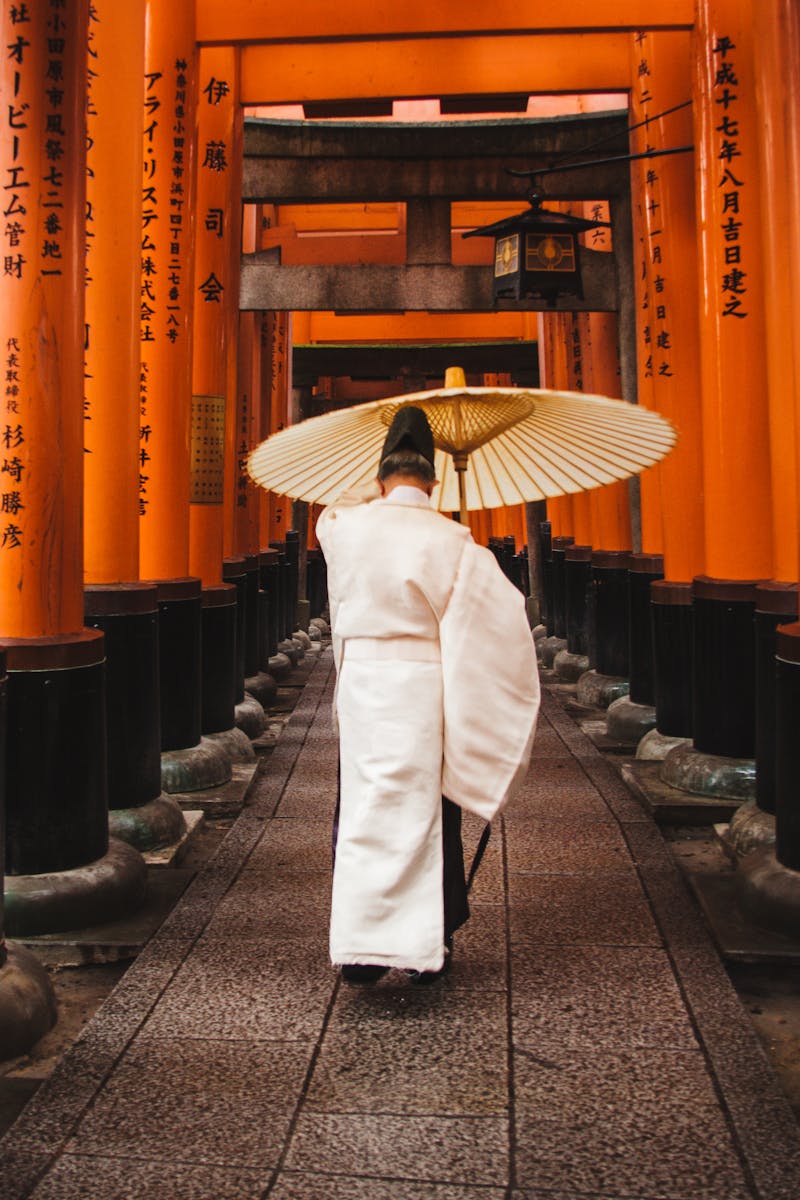 A person in traditional attire walks through the iconic torii gates at Fushimi Inari Shrine, Kyoto.